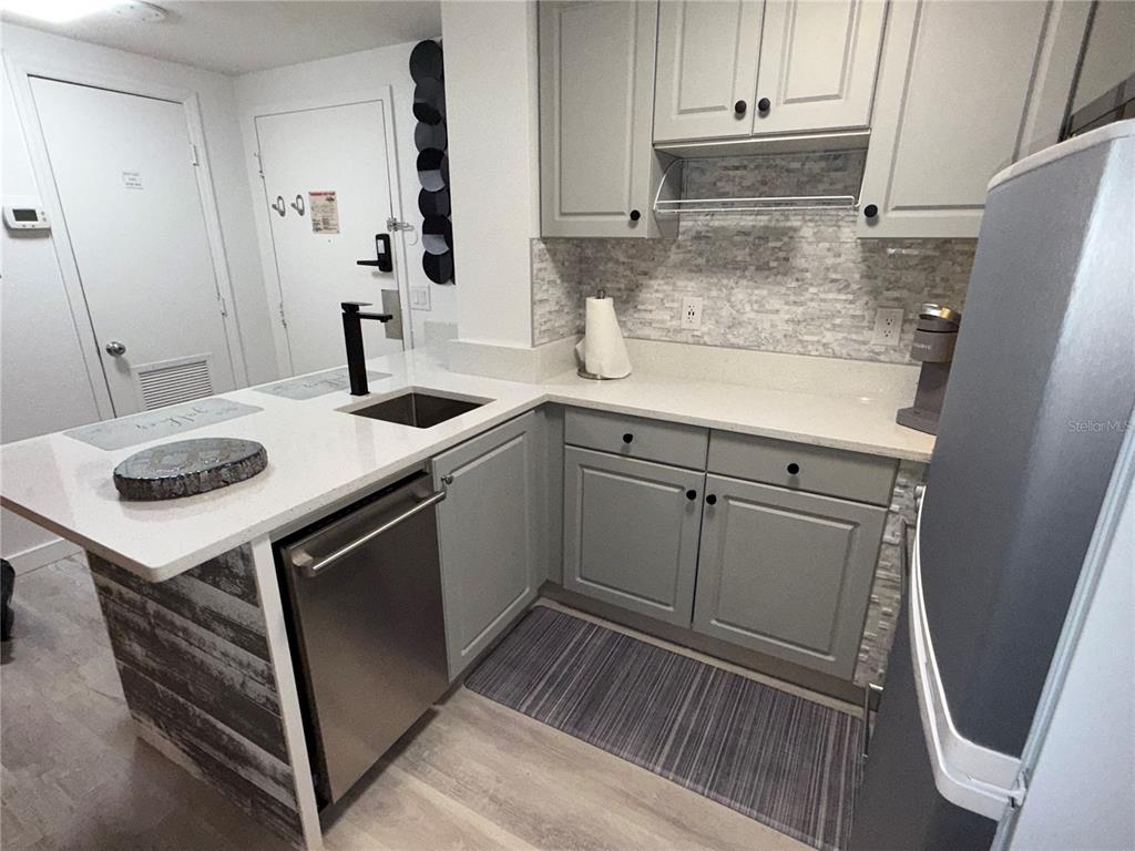 A kitchen features light gray cabinets, white countertops, a stainless steel dishwasher, and tiled backsplash — 6165 CARRIER DRIVE UNIT 3106, ORLANDO, FL