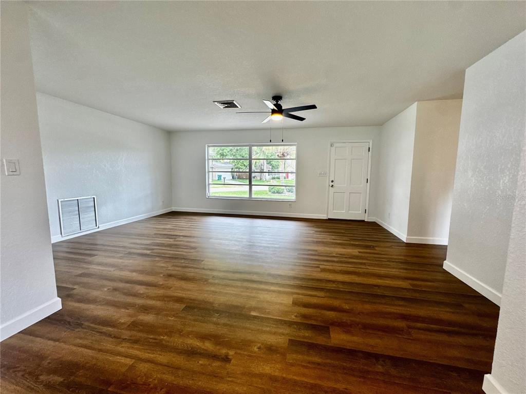 An empty living room features wood-look flooring, white walls, a ceiling fan, and a front door — 12620 82ND TERRACE, SEMINOLE, FL