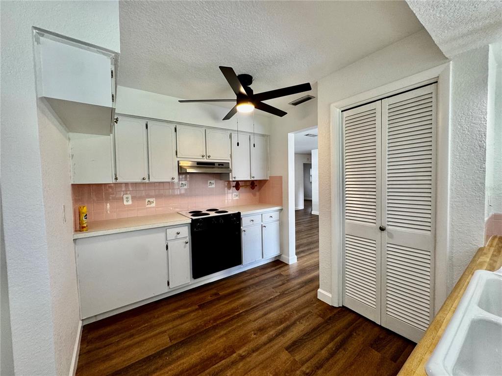 A kitchen with white cabinets, a black stove, pink tile backsplash, and wood-look flooring — 12620 82ND TERRACE, SEMINOLE, FL