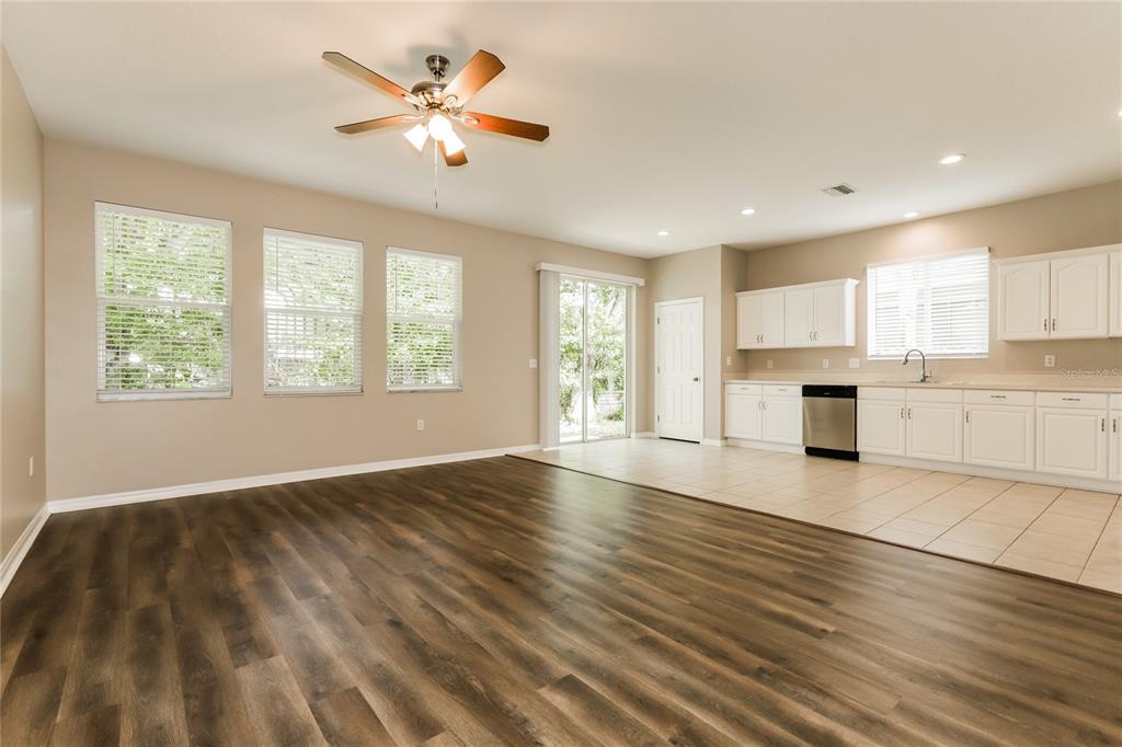 An open-concept room with wood-look flooring, a ceiling fan, and an adjacent tiled kitchen area — 1035 CLEARPOINTE WAY, LAKELAND, FL