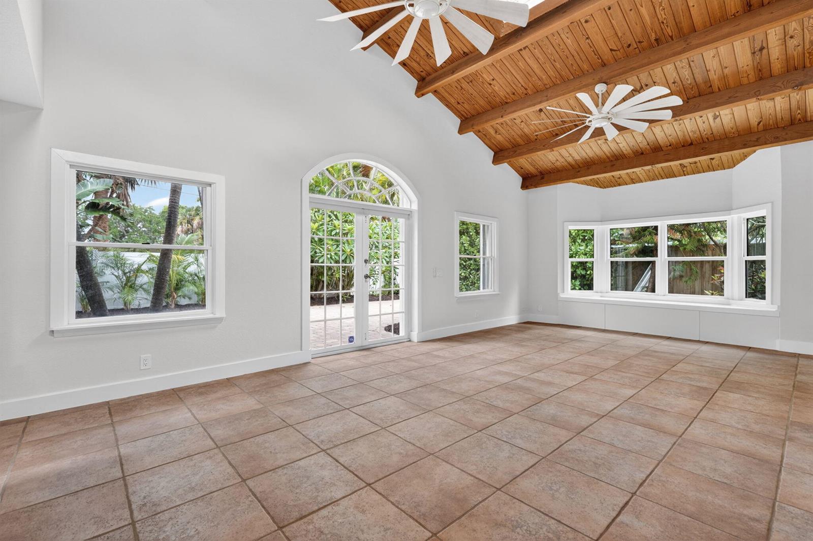 A bright, empty room features a vaulted wood-beam ceiling, tile flooring, and large windows — 606 Paulina Road, Jupiter FL 33477, JUPITER, FL