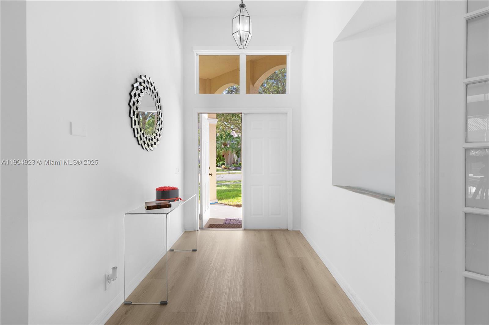 A bright entryway features light wood flooring, a glass console table, and a circular mirror — 1102 Camellia Cir, Weston FL 33326, WESTON, FL