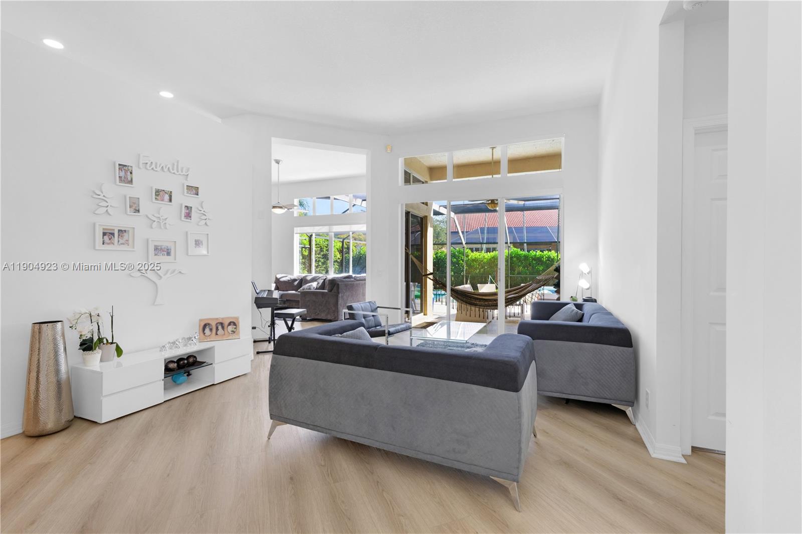 A bright living room features light wood flooring, white walls, and glass sliding doors — 1102 Camellia Cir, Weston FL 33326, WESTON, FL