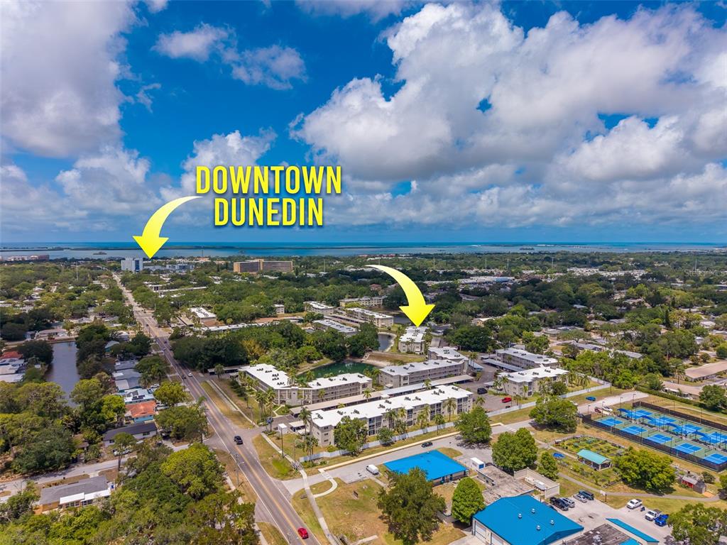 This aerial view shows apartment complexes, a road, and tennis courts near the coast — 946 VIRGINIA STREET UNIT 107, DUNEDIN, FL
