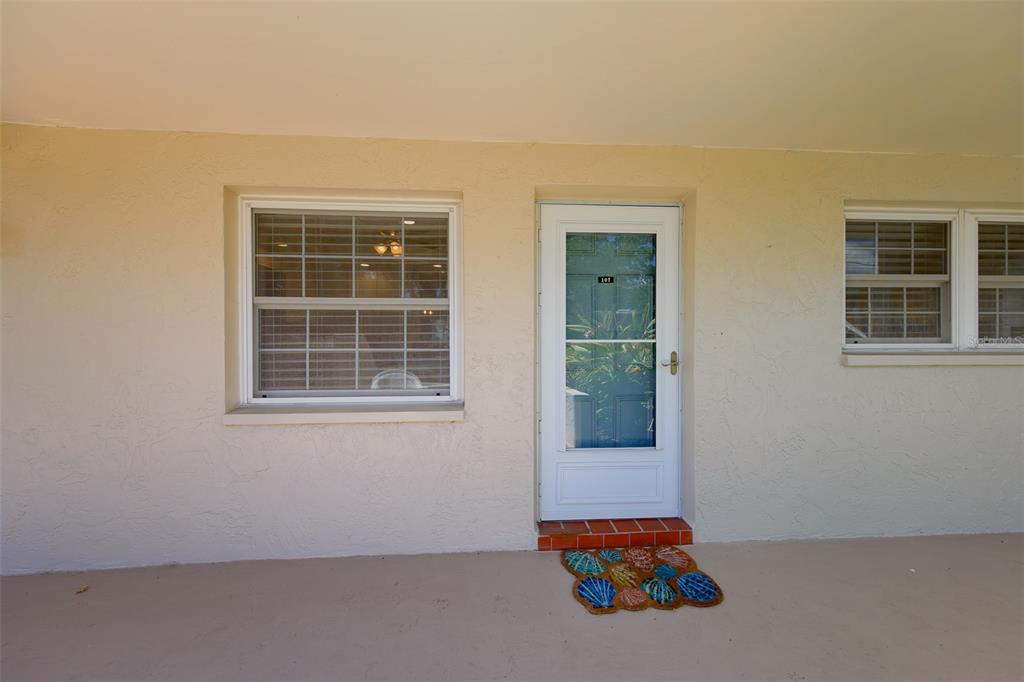A beige exterior wall features a white front door and two windows with shutters — 946 VIRGINIA STREET UNIT 107, DUNEDIN, FL