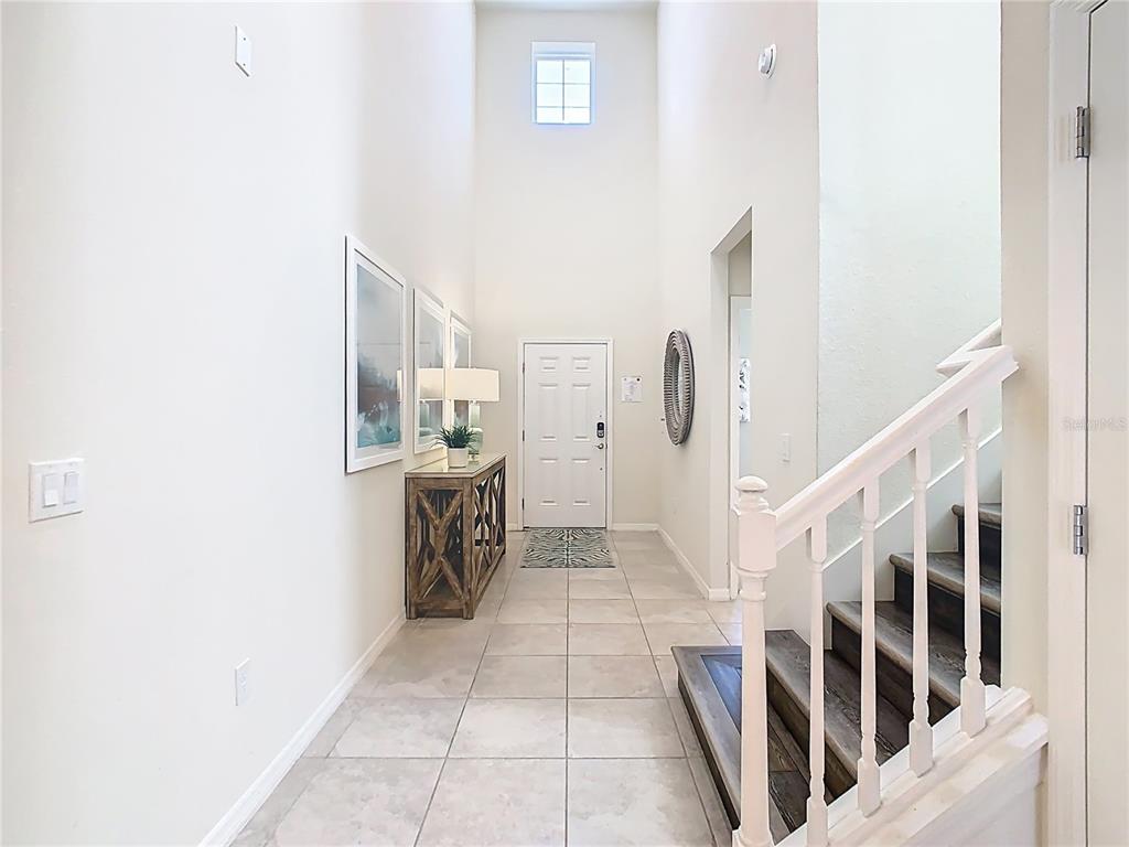 A high-ceilinged entryway features tile flooring, a wooden console table, and a staircase — 4125 LANA AVENUE, DAVENPORT, FL