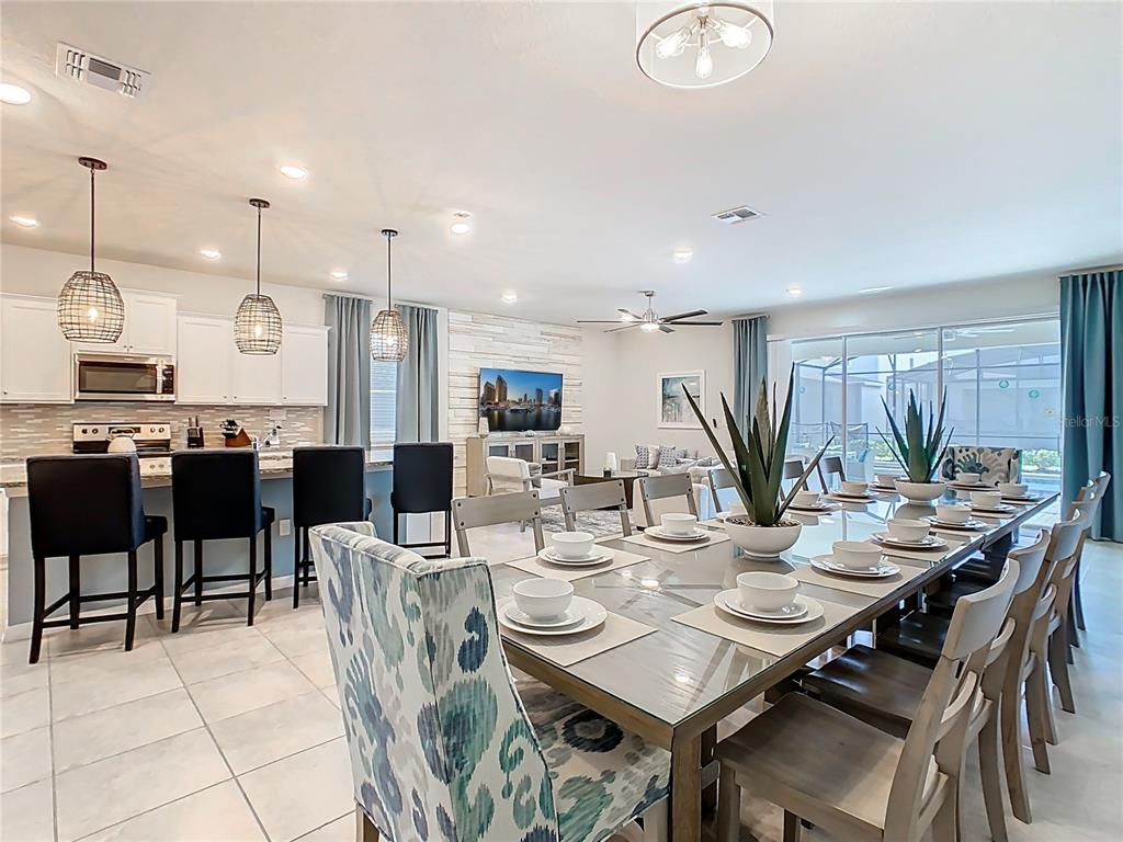 An open-concept kitchen and dining area features a long glass table, bar seating, and tile flooring — 4125 LANA AVENUE, DAVENPORT, FL
