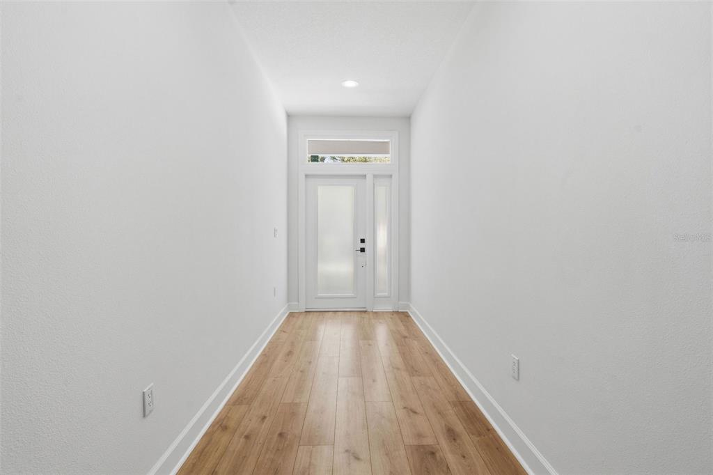 A bright entryway features light wood-look flooring, white walls, and a modern glass-paneled front door — 2617 E PALIFOX STREET, TAMPA, FL