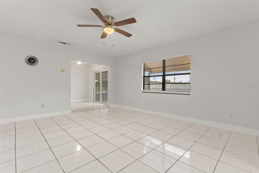 A bright, tiled living room features a ceiling fan, a large window, and an adjacent room — 4506 24TH AVENUE S, TAMPA, FL