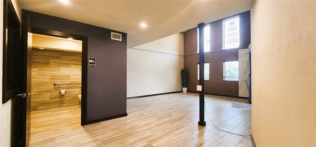 A spacious room with wood-look tile flooring, a restroom entrance, and tall windows — 251 E PARK AVENUE UNIT 102, LAKE WALES, FL