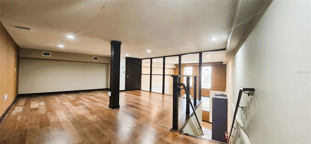 An open loft area features hardwood floors, a dark support pillar, and a glass-paneled railing — 251 E PARK AVENUE UNIT 102, LAKE WALES, FL