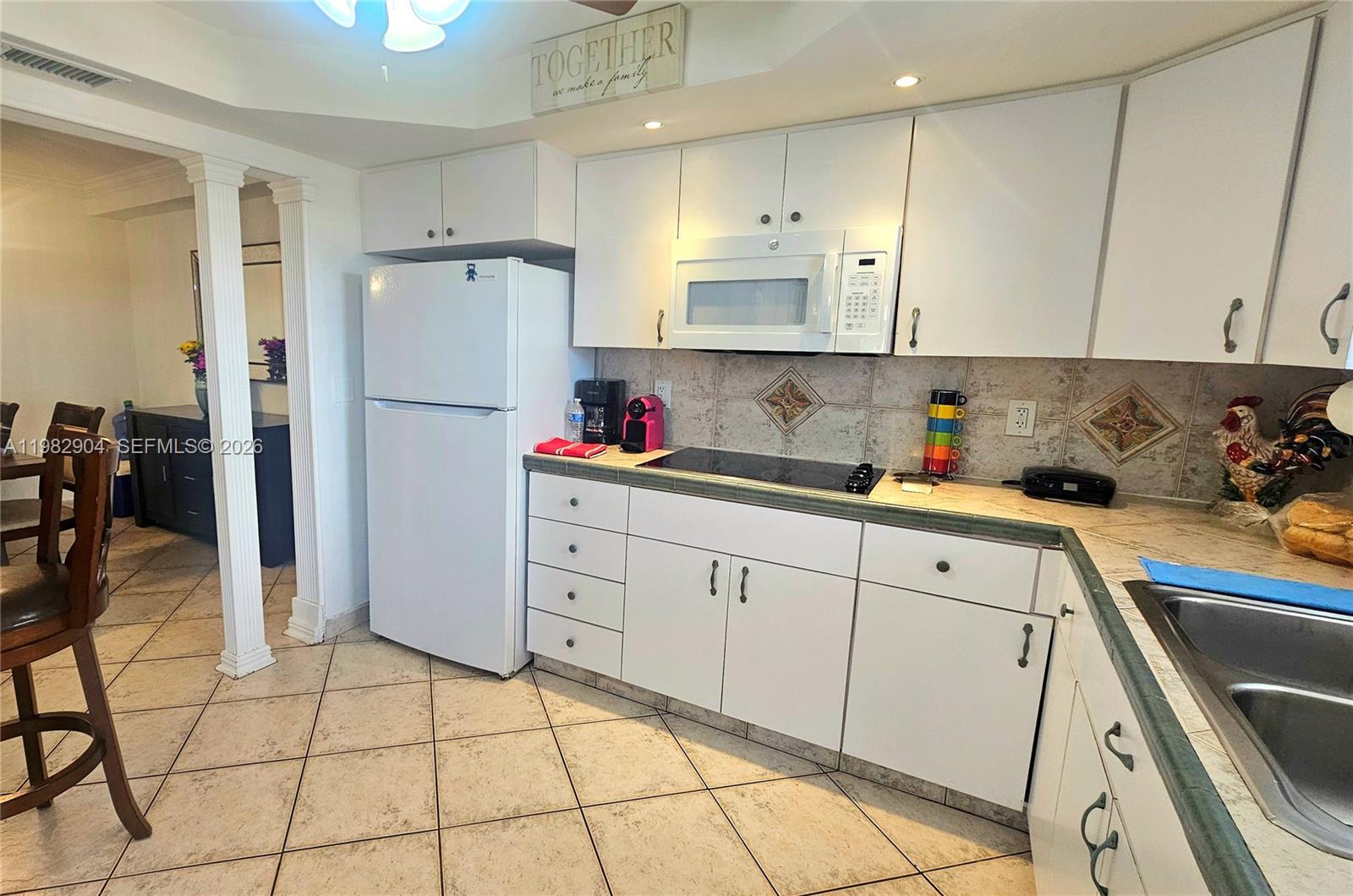 A kitchen features white cabinets, a white refrigerator, a glass cooktop, and tiled flooring — 180 NE 12th Ave # 10E, Hallandale Beach FL 33009, HALLANDALE BEACH, FL