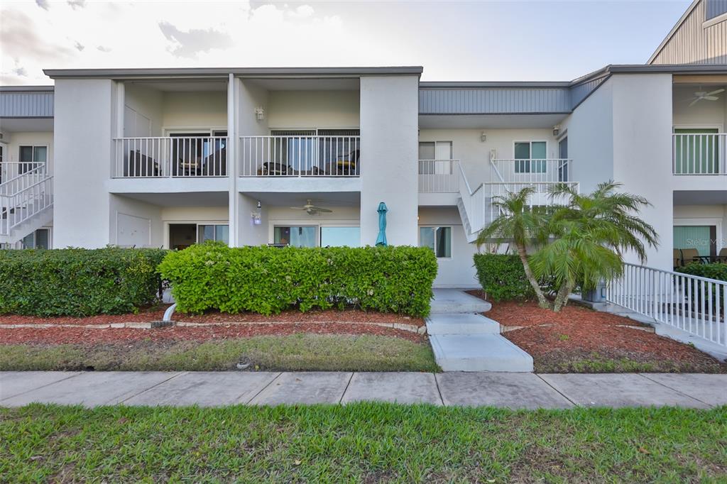 Exterior view of a two-story apartment building with balconies, a hedge, and a walkway — 14800 WALSINGHAM ROAD UNIT 1203, LARGO, FL