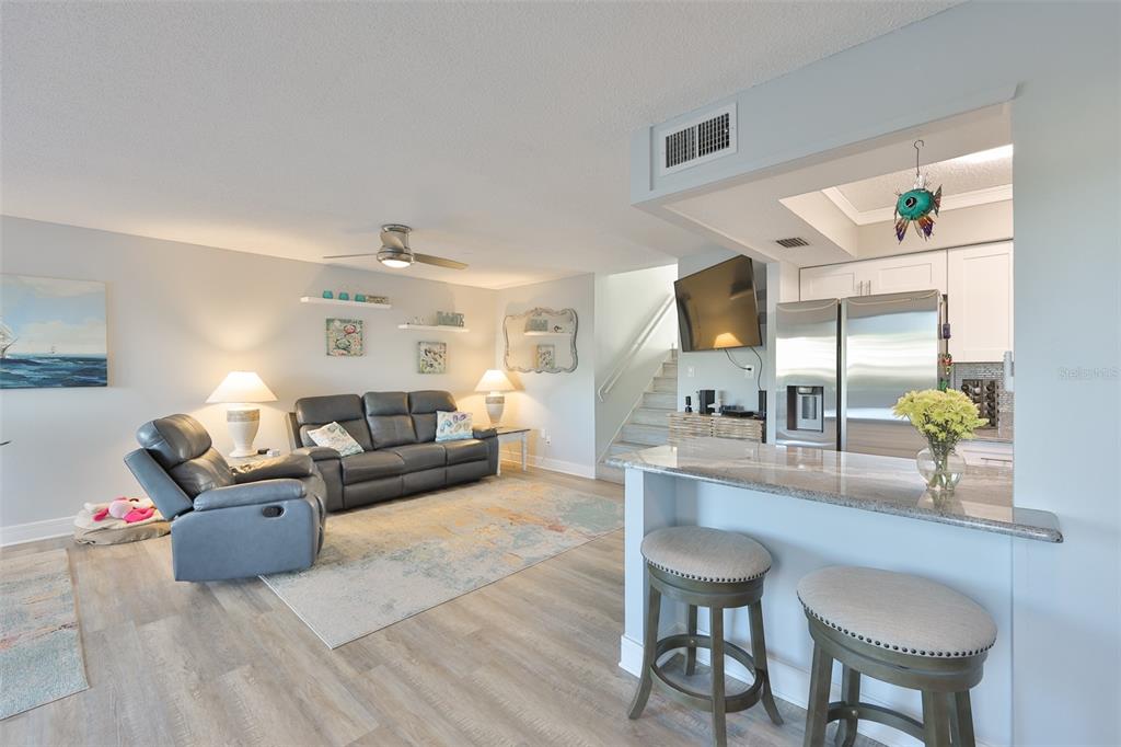 A living room with a gray sofa and recliner opens to a kitchen with bar seating — 14800 WALSINGHAM ROAD UNIT 1203, LARGO, FL