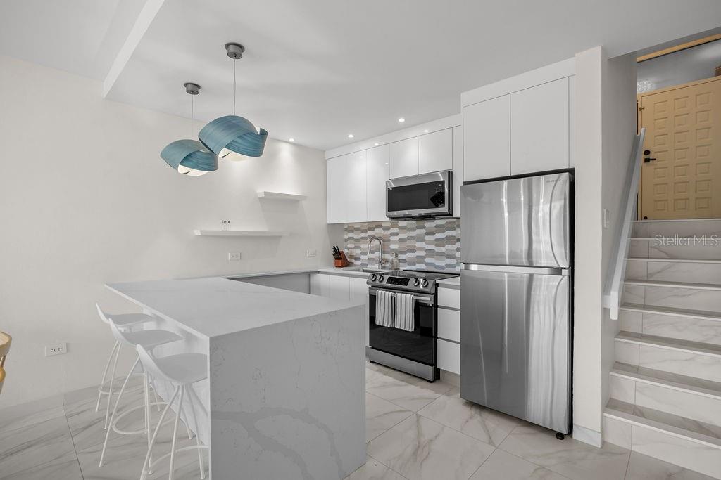 A modern kitchen features white cabinetry, stainless steel appliances, a quartz island, and tiled flooring — 310 BEACH VILLAGE DRIVE, HUMACAO, PR