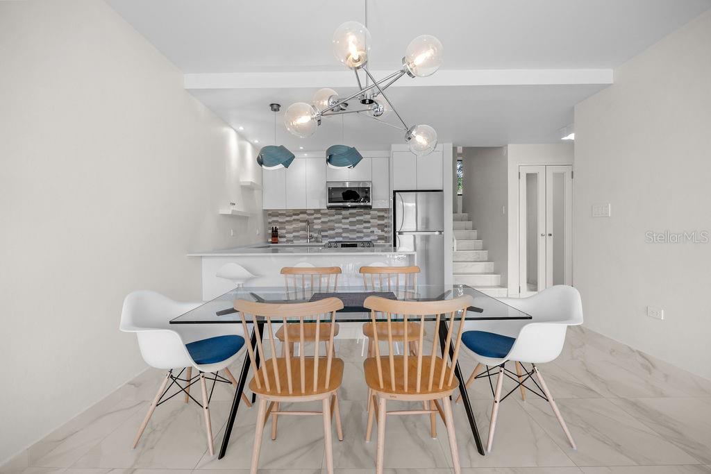 A modern dining area features a glass table, wooden chairs, and an adjacent open kitchen — 310 BEACH VILLAGE DRIVE, HUMACAO, PR