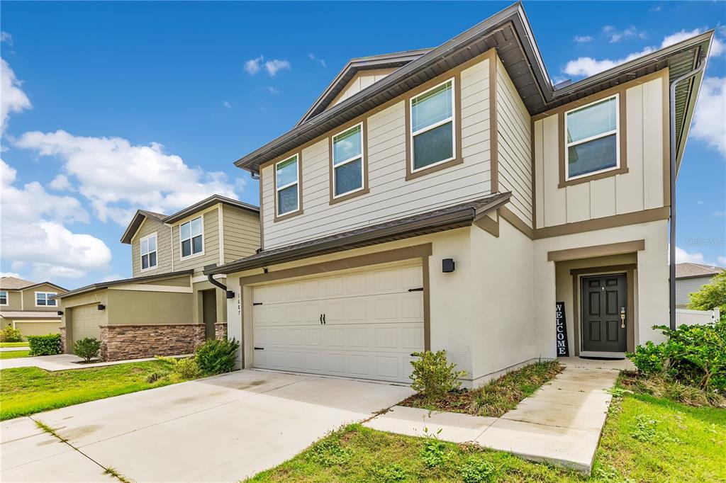 A two-story suburban house with a beige stucco exterior, a two-car garage, and a front entrance — 1687 BEAR MOUNTAIN LANE, MINNEOLA, FL