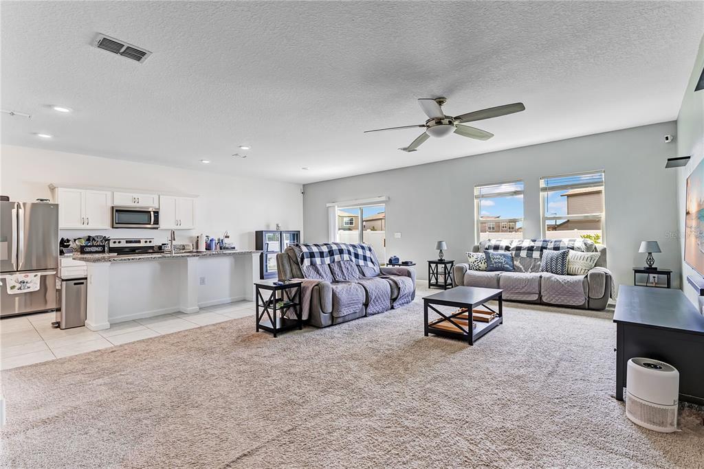 An open-concept living room and kitchen featuring carpeted floors, neutral walls, and a ceiling fan — 1687 BEAR MOUNTAIN LANE, MINNEOLA, FL