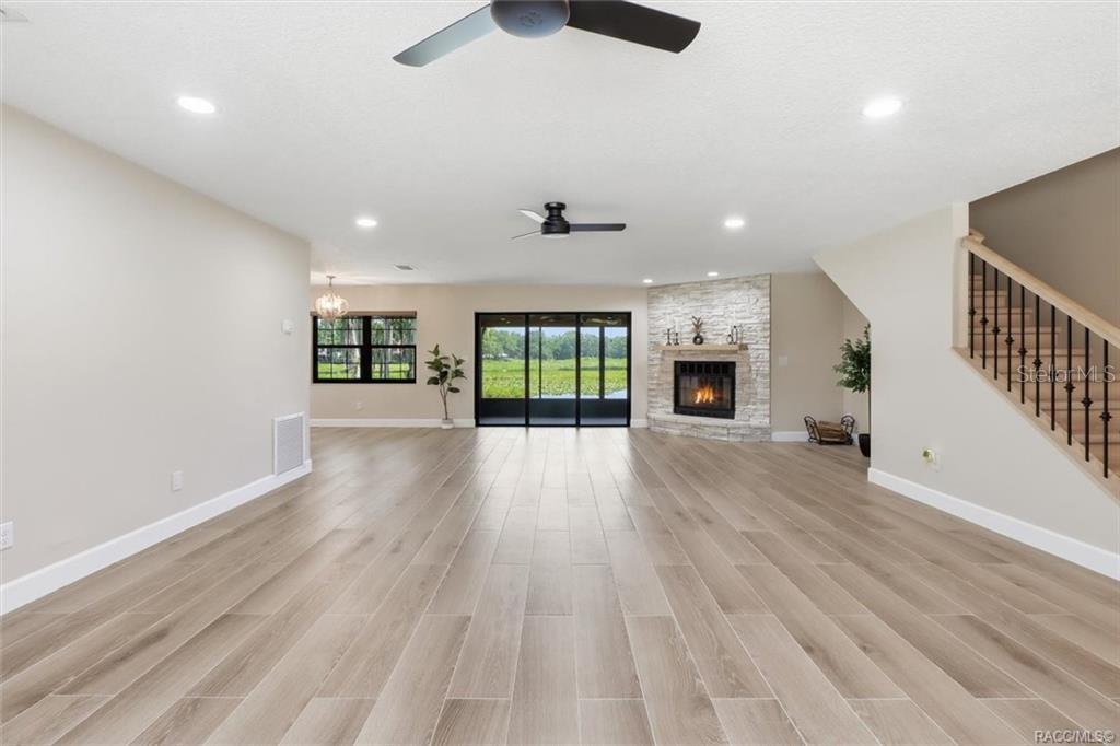 A spacious living room features light wood-look tile flooring, a stone fireplace, and sliding doors — 1425 S HOMESTEAD POINT, INVERNESS, FL