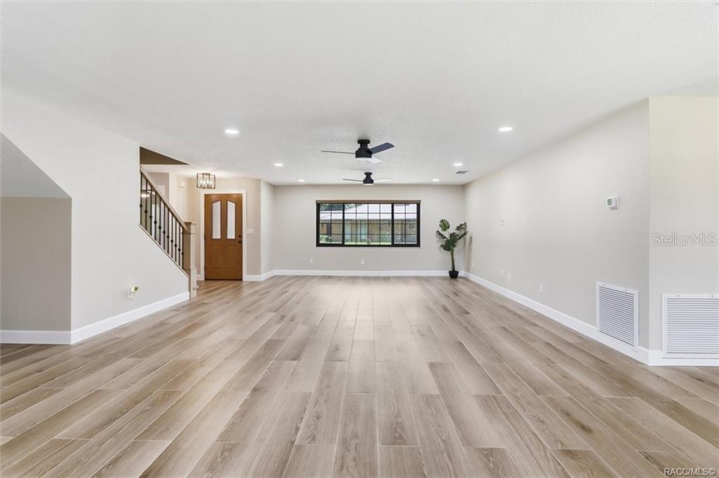A spacious, empty room features light wood-look flooring, white walls, a staircase, and a window — 1425 S HOMESTEAD POINT, INVERNESS, FL