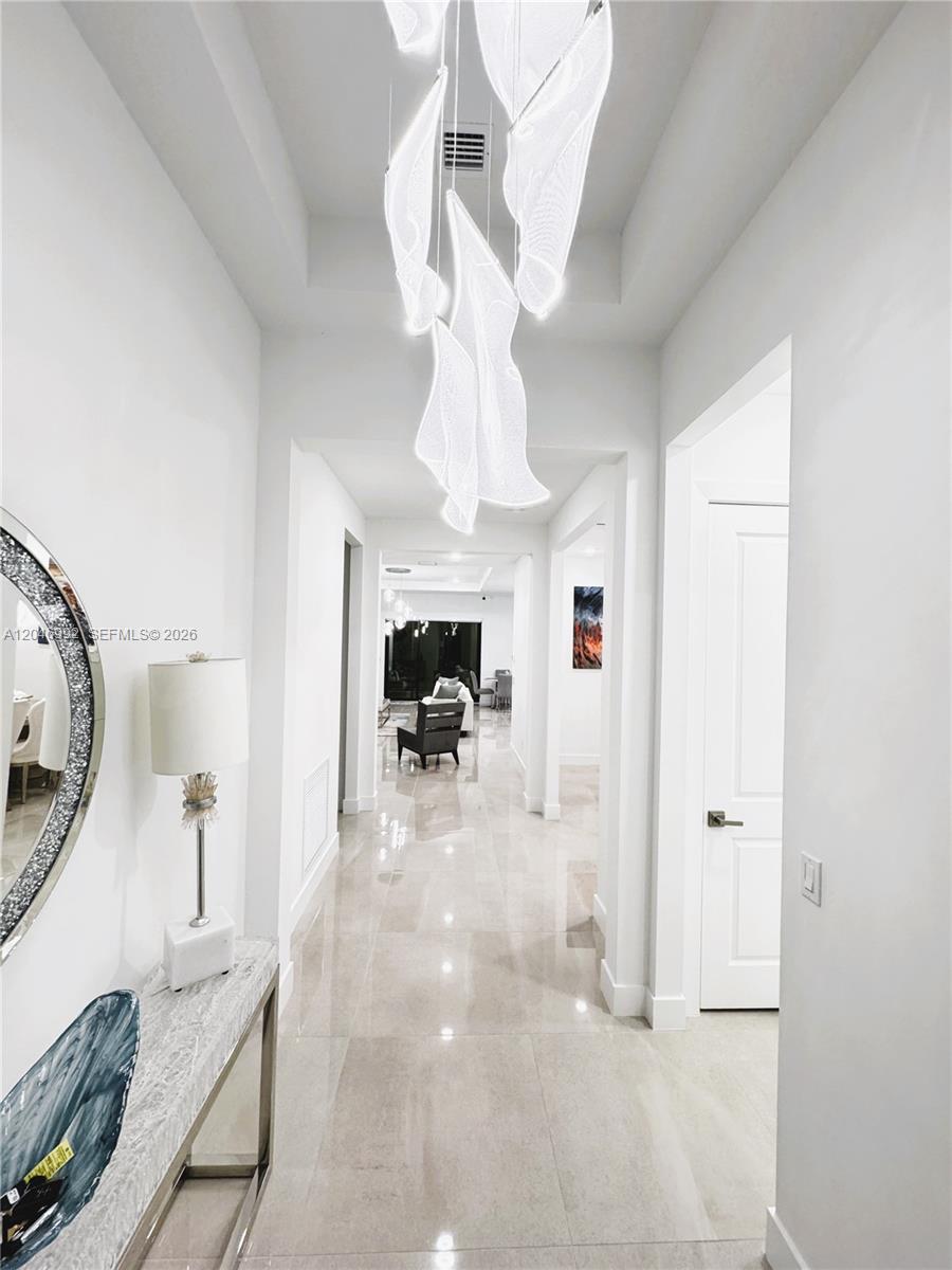 A bright hallway features a modern sculptural chandelier, polished tile floors, and white walls — 5444 SW Saint Armands Way, Westlake FL 33470, WESTLAKE, FL
