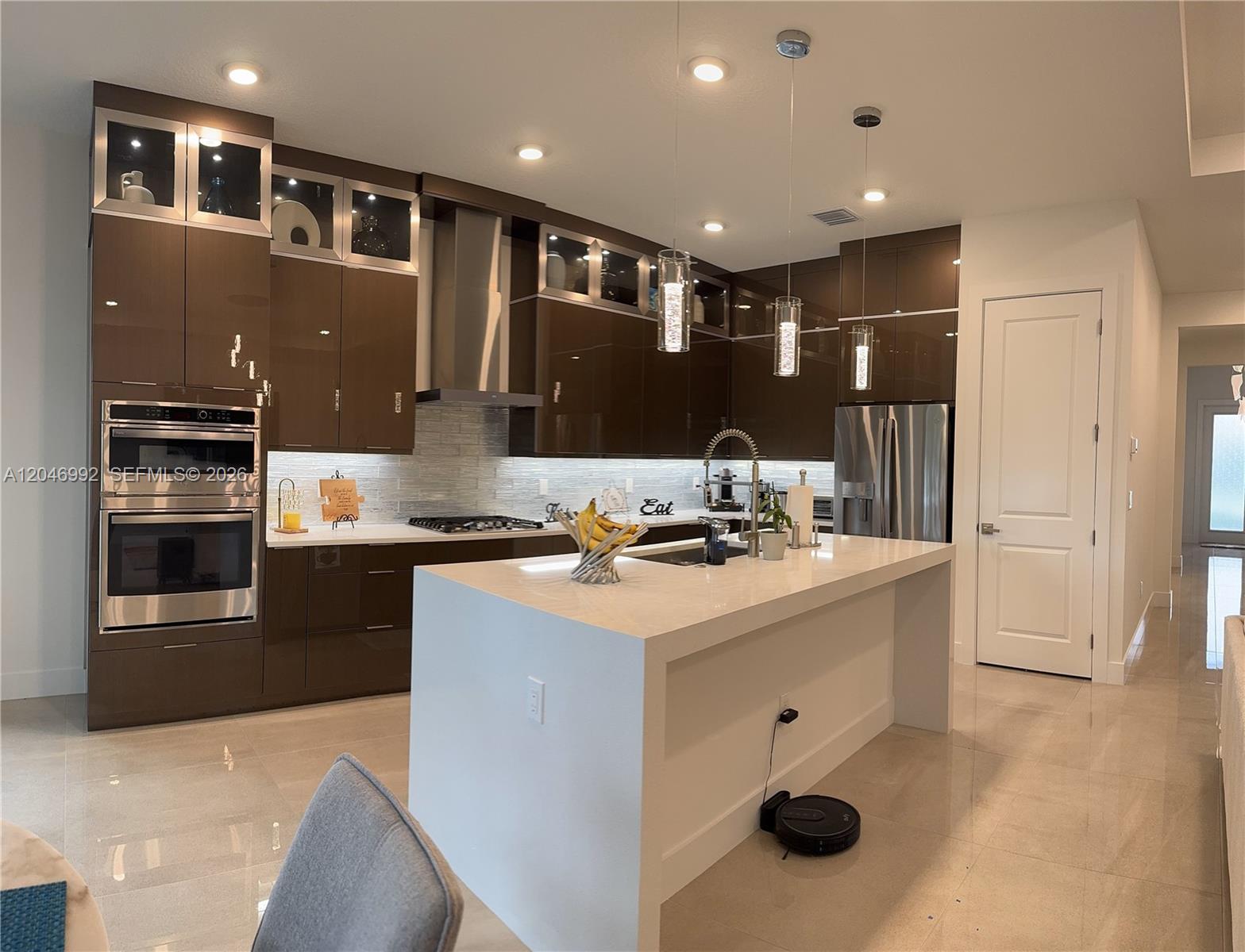 A modern kitchen features dark glossy cabinets, a white waterfall island, and stainless steel appliances — 5444 SW Saint Armands Way, Westlake FL 33470, WESTLAKE, FL