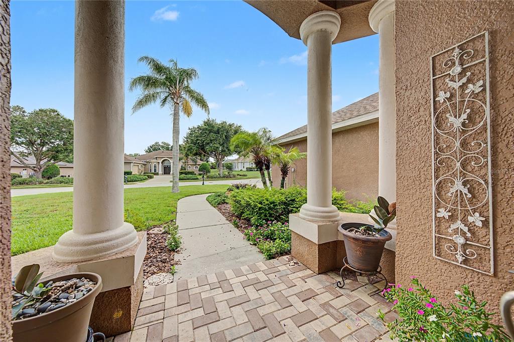 A view from a covered porch looking out toward a sidewalk, lawn, and neighboring houses — 13301 THOROUGHBRED DRIVE, DADE CITY, FL