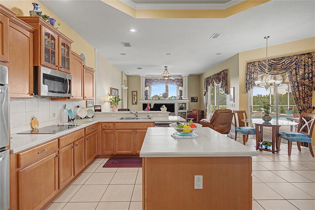 A kitchen with wood cabinets, white countertops, and an island opens to a living area — 13301 THOROUGHBRED DRIVE, DADE CITY, FL