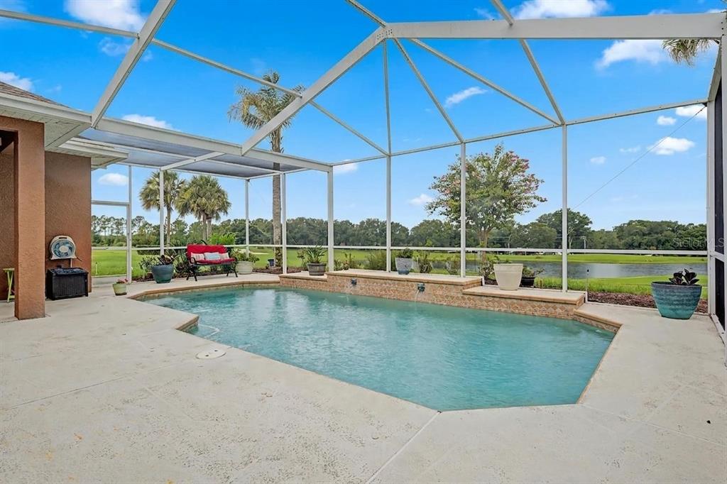 A screened-in patio features a swimming pool with a water feature and a lake view — 13301 THOROUGHBRED DRIVE, DADE CITY, FL