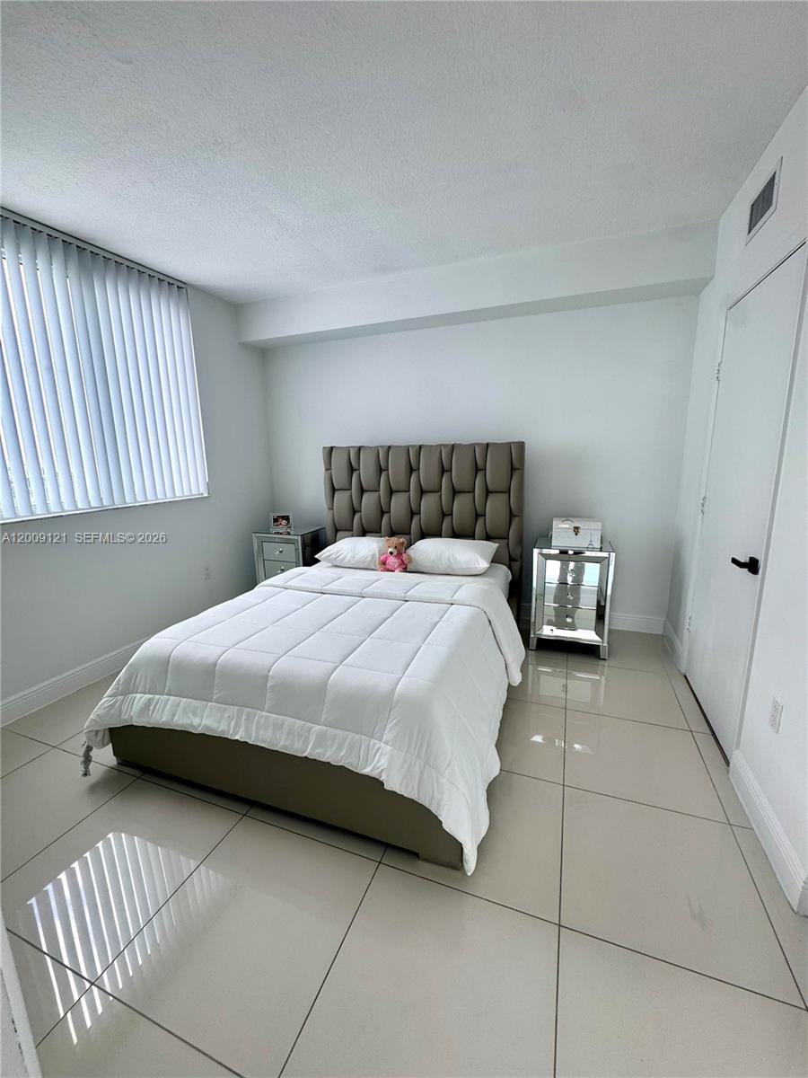 A bedroom features a tufted headboard, a white bedspread, and light-colored tile flooring — 1871 NW S River Dr # 2005, Miami FL 33125, MIAMI, FL
