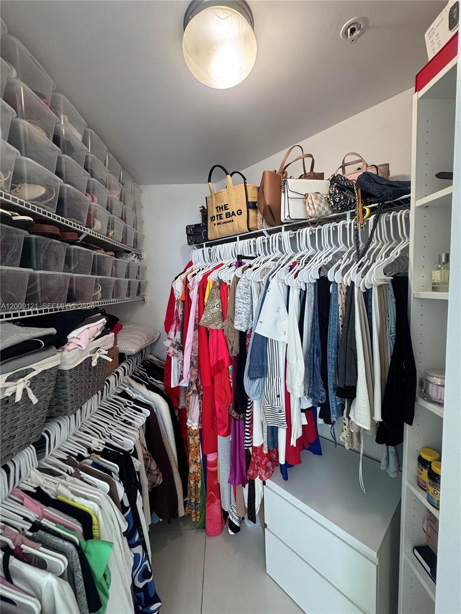 A walk-in closet features white shelving, hanging clothes, clear storage bins, and a central light fixture — 1871 NW S River Dr # 2005, Miami FL 33125, MIAMI, FL