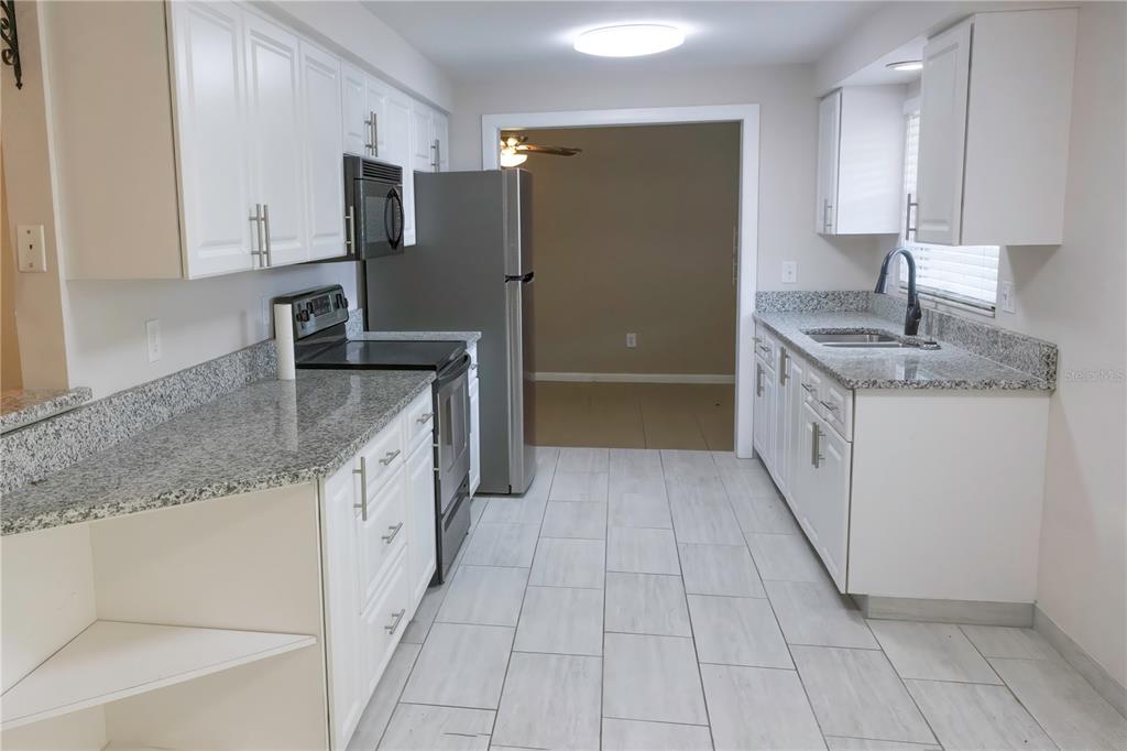 A kitchen with white cabinets, granite countertops, stainless steel appliances, and light-colored tile flooring — 5333 DUNCANWOOD DRIVE, SARASOTA, FL