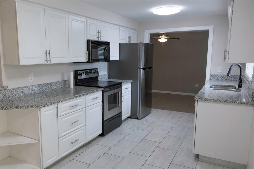 A kitchen features white cabinets, granite countertops, stainless steel appliances, and light-colored tile flooring — 5333 DUNCANWOOD DRIVE, SARASOTA, FL