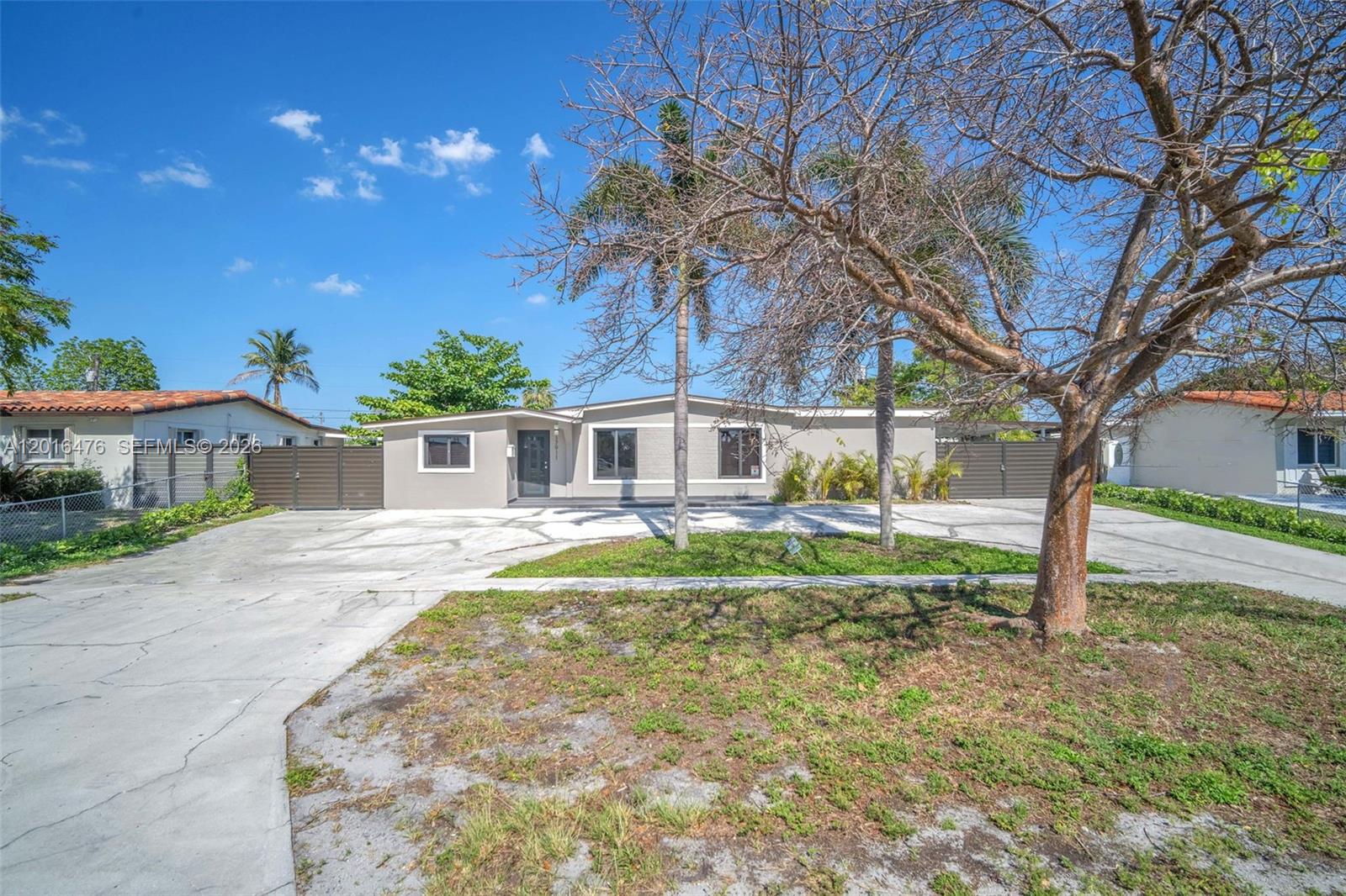 A single-story house with a concrete driveway and palm trees sits under a blue sky — 17911 NW 82nd Ave, Hialeah FL 33015, HIALEAH, FL