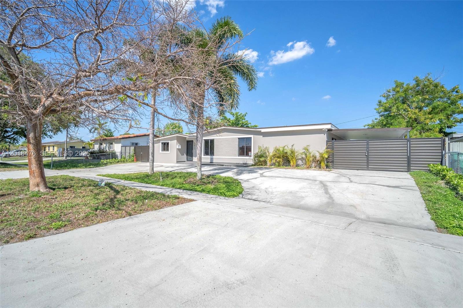 A single-story house with a large concrete driveway, palm trees, and a gated side entrance — 17911 NW 82nd Ave, Hialeah FL 33015, HIALEAH, FL