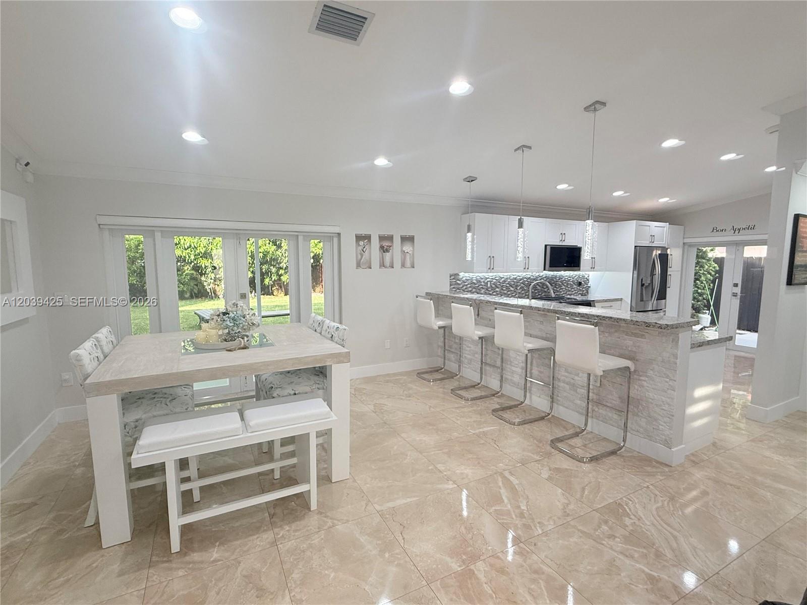 A bright kitchen features white cabinetry, a stone-topped breakfast bar, and a dining area — 19331 NW 57th Ct, Miami FL 33015, MIAMI, FL