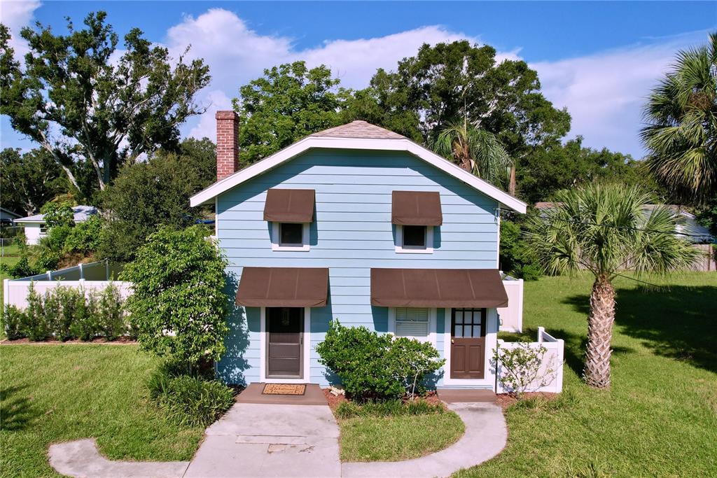 A two-story light blue house with brown awnings and a brick chimney stands on grass — 363 14TH STREET NW, LARGO, FL