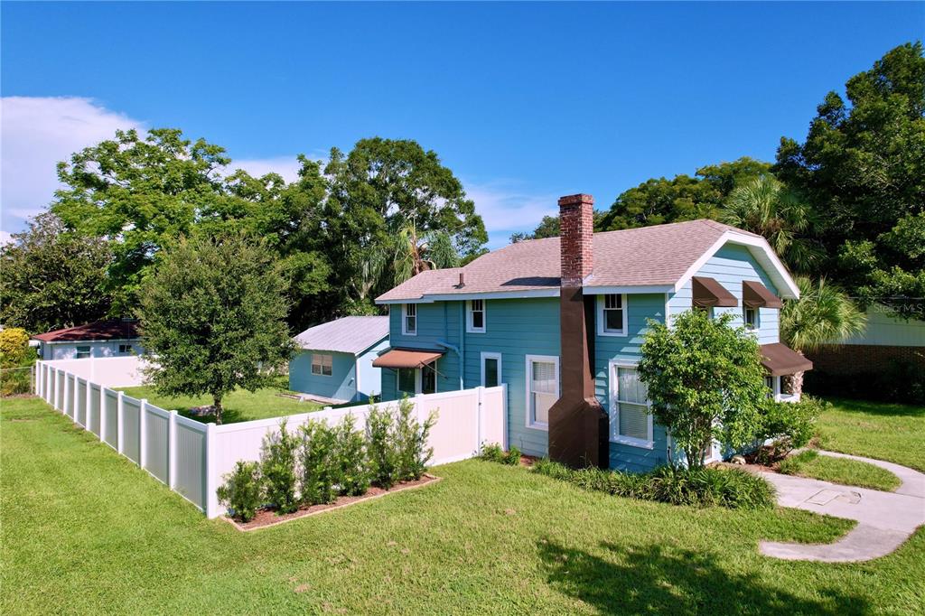 A two-story teal house with a brick chimney and a white vinyl fence in the yard — 363 14TH STREET NW, LARGO, FL
