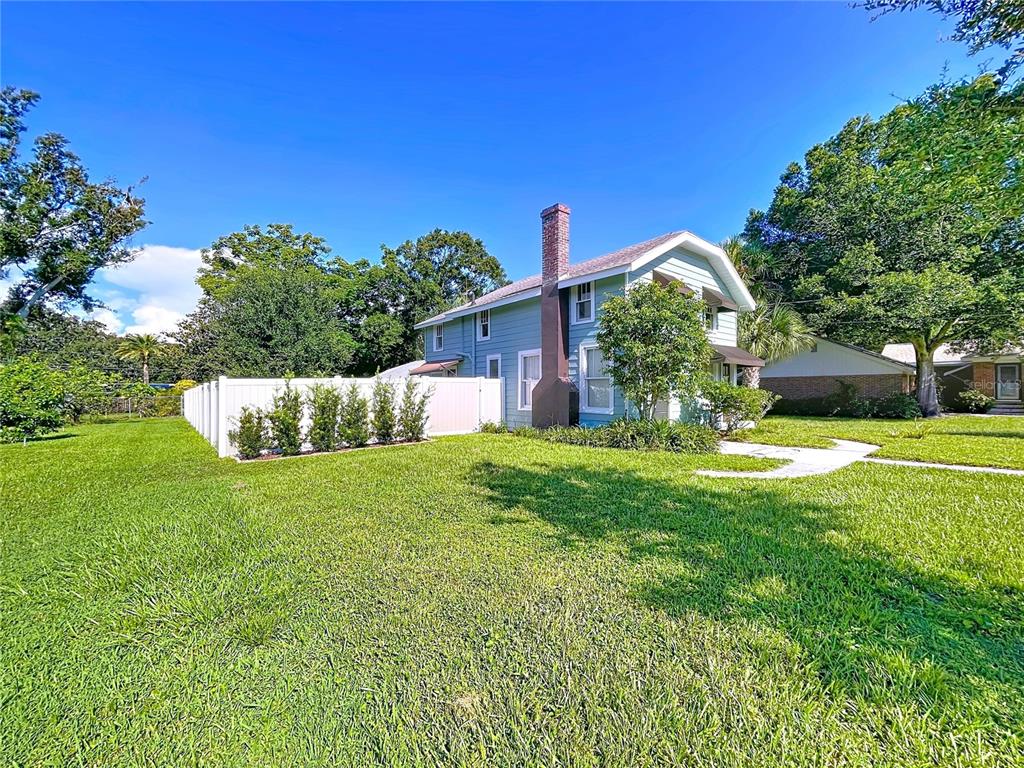 A light blue two-story house with a brick chimney stands on a grassy lawn — 363 14TH STREET NW, LARGO, FL