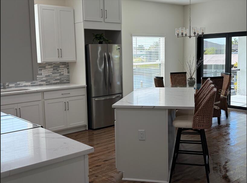 A modern kitchen features white cabinetry, stainless steel appliances, and a marble-topped island with seating — 6203 BOLANDER TERRACE Lot 3, NORTH PORT, FL