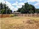A flat, grassy vacant lot is enclosed by a wooden fence with trees in the background — 2507 CORAL WAY, LAKELAND, FL