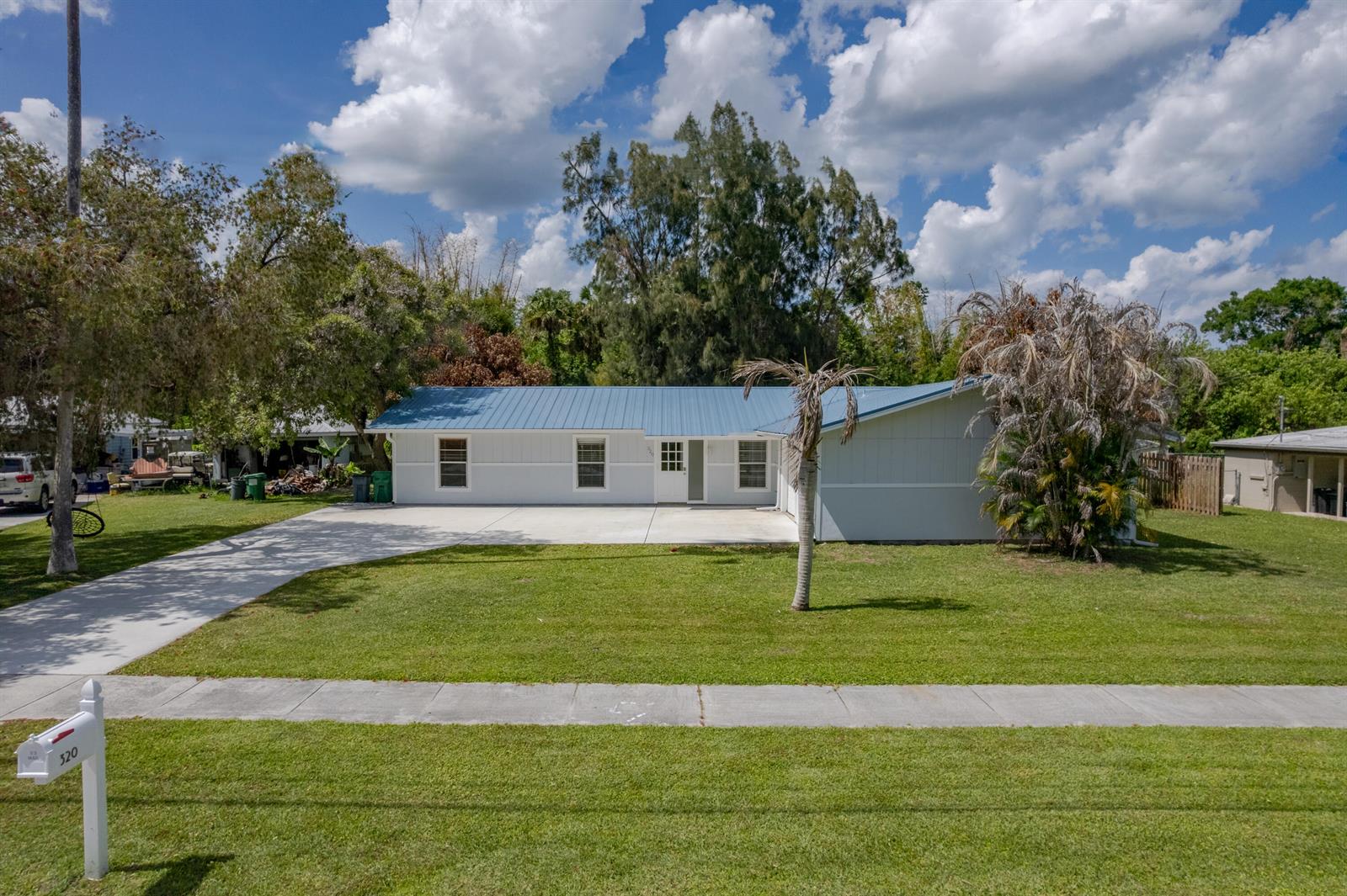 A single-story house with a blue metal roof and a concrete driveway sits on grass — 320 Chamberlain Boulevard, Fort Pierce FL 34946, FORT PIERCE, FL