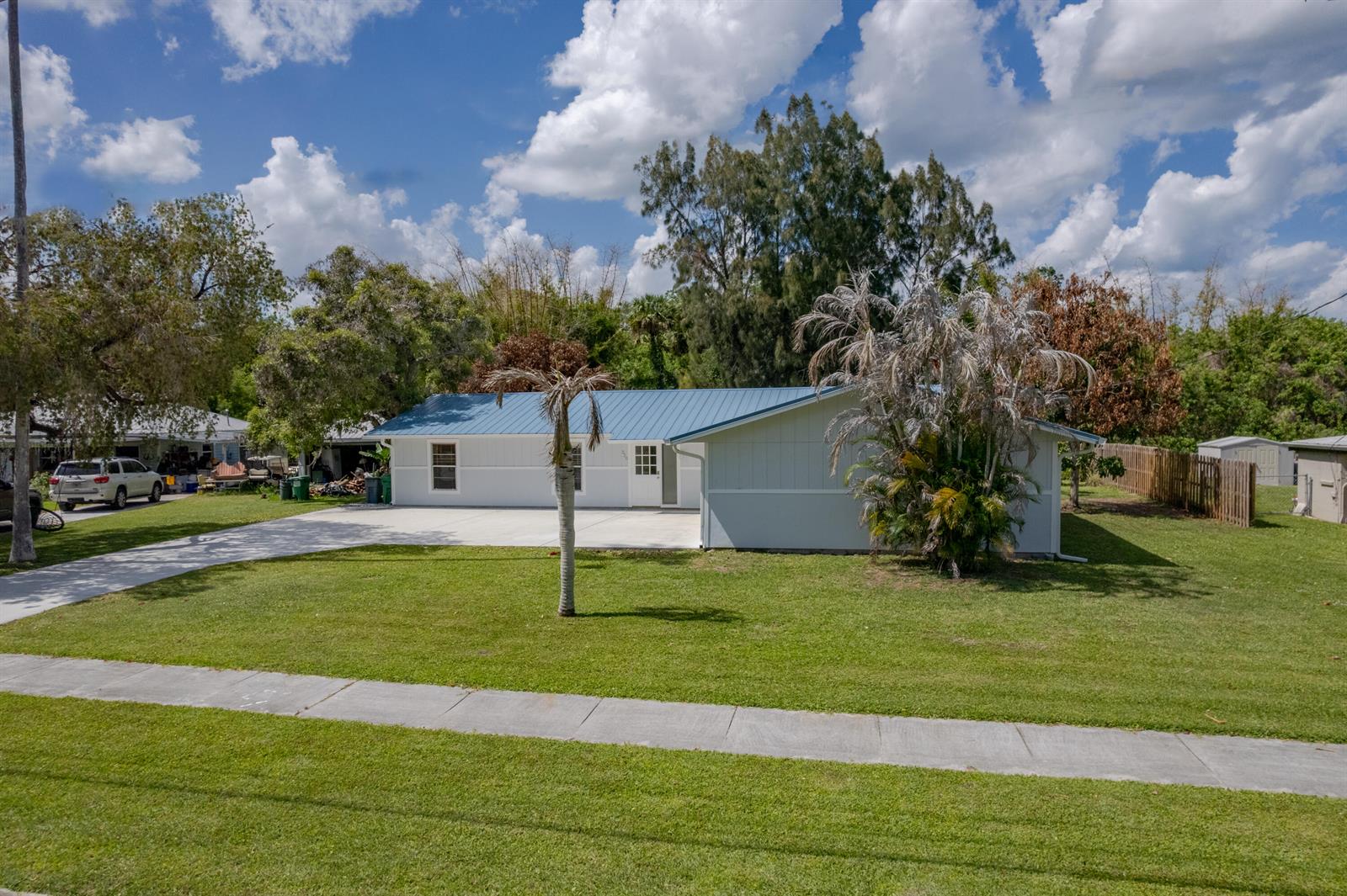 A single-story white house with a blue metal roof sits on a grassy lot — 320 Chamberlain Boulevard, Fort Pierce FL 34946, FORT PIERCE, FL