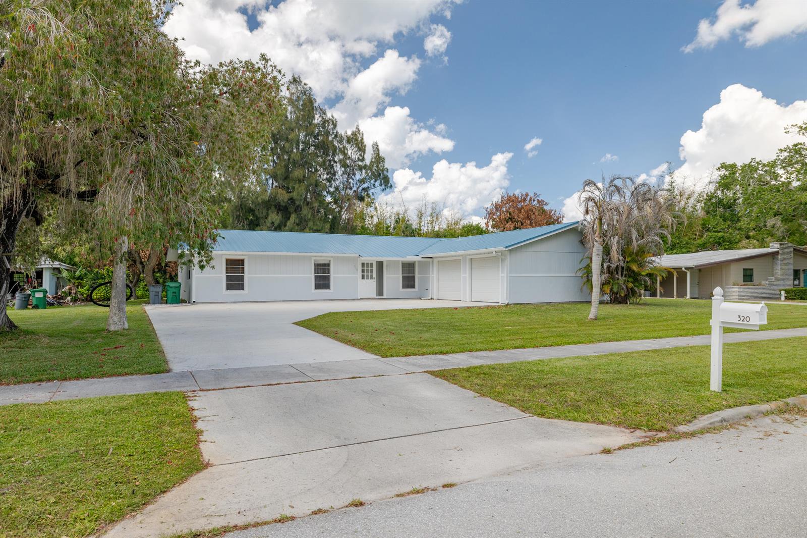 A light-colored single-story house with a blue metal roof and an attached two-car garage — 320 Chamberlain Boulevard, Fort Pierce FL 34946, FORT PIERCE, FL