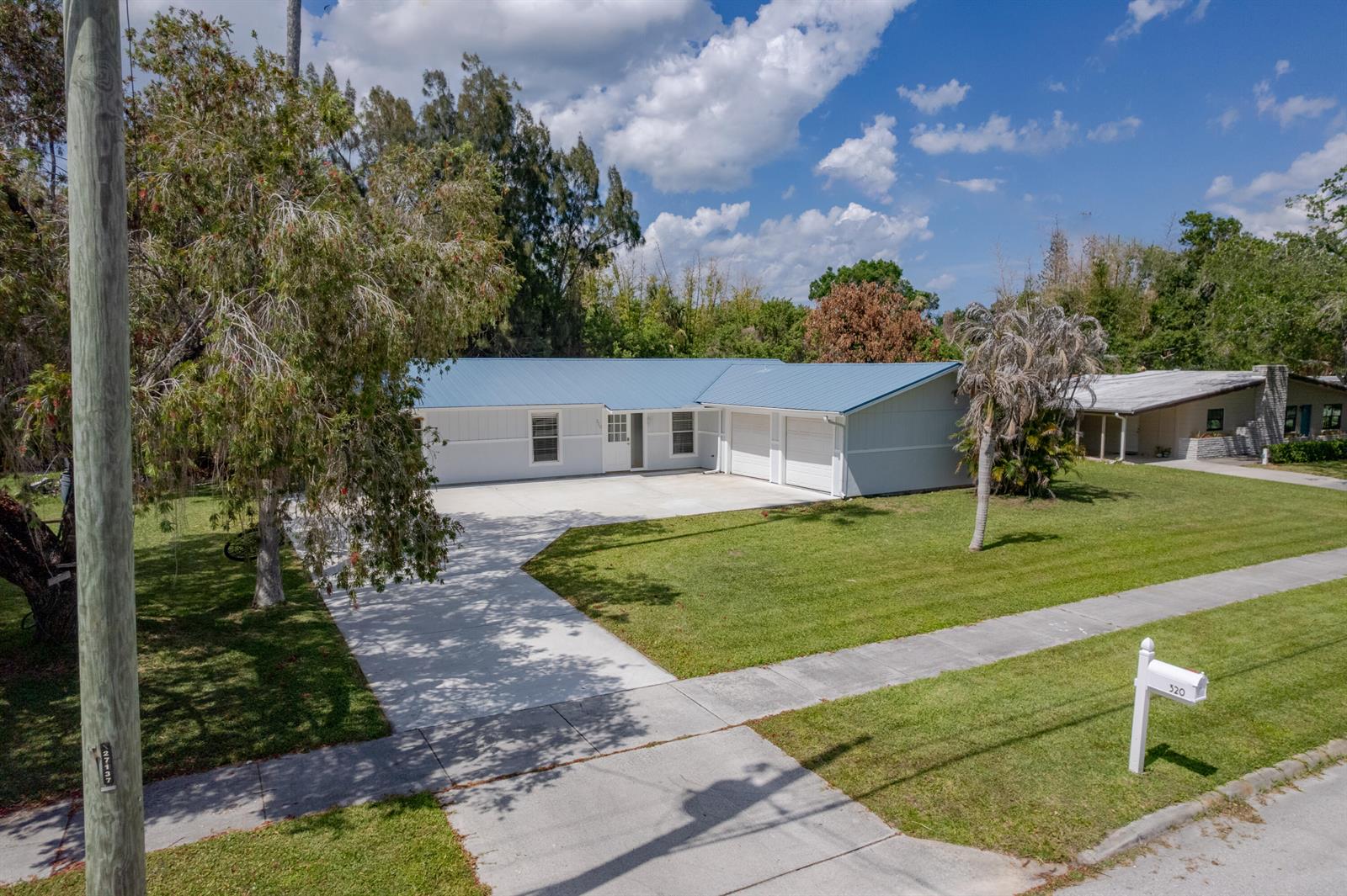 An exterior view of a single-story house with a blue metal roof and driveway — 320 Chamberlain Boulevard, Fort Pierce FL 34946, FORT PIERCE, FL