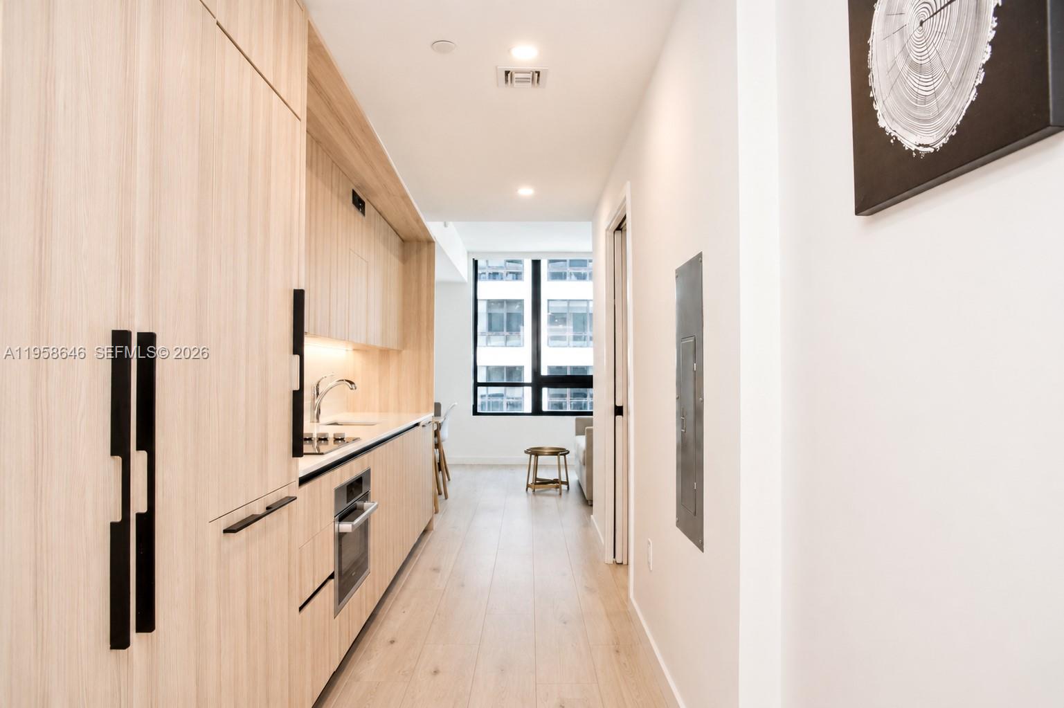 A narrow kitchen features light wood cabinetry, stainless steel appliances, and light wood flooring — 225 N Miami Ave # 2508, Miami FL 33128, MIAMI, FL