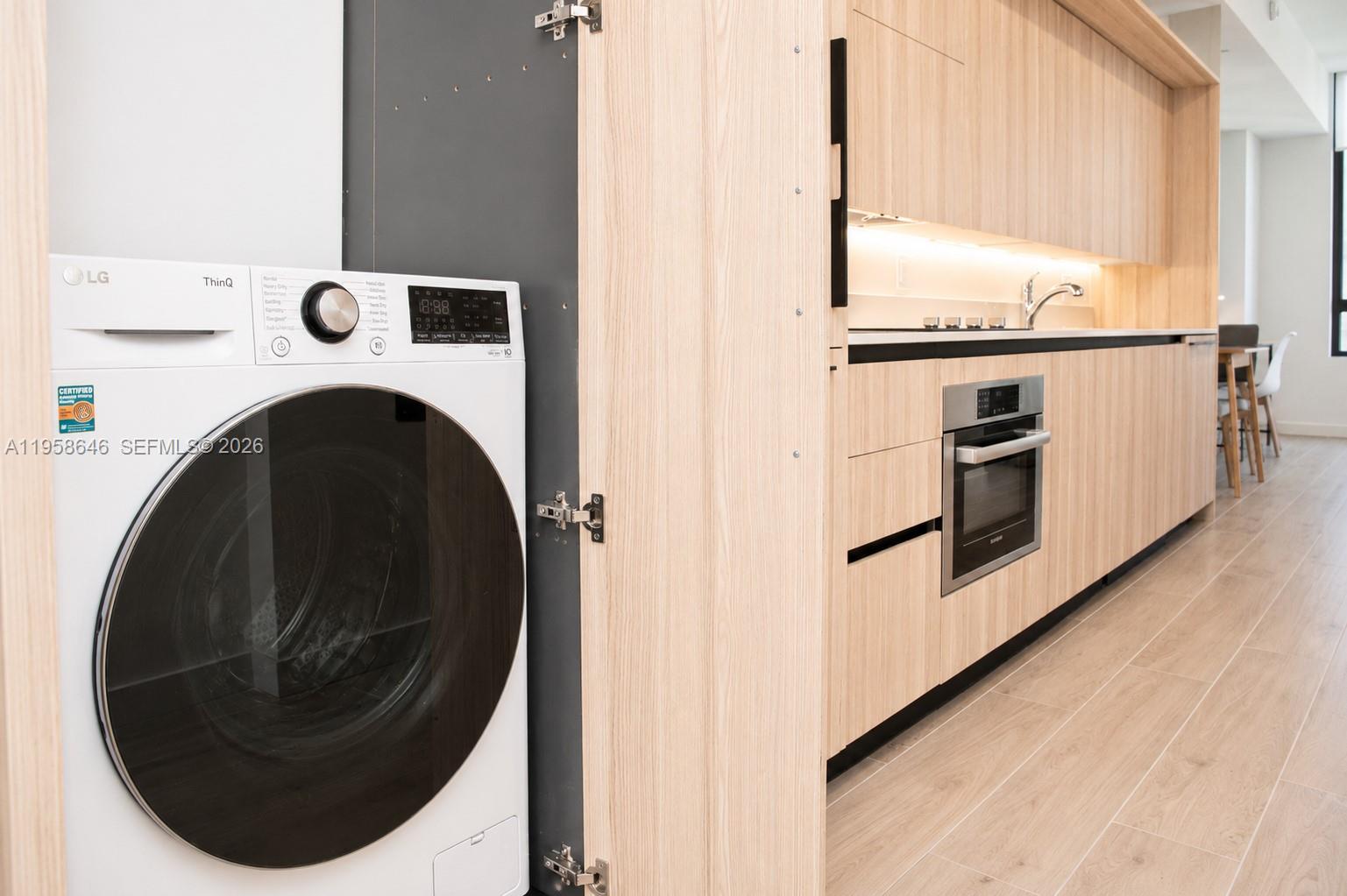A modern kitchen features light wood cabinetry, a built-in oven, and an adjacent laundry closet — 225 N Miami Ave # 2508, Miami FL 33128, MIAMI, FL