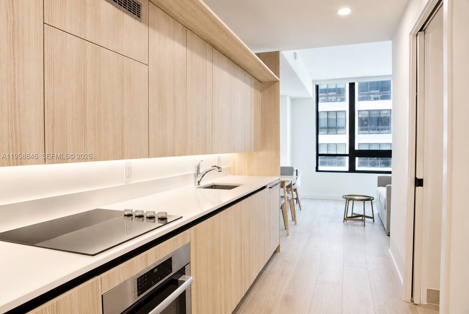 A modern kitchen features light wood cabinetry, white countertops, and a built-in oven — 225 N Miami Ave # 2508, Miami FL 33128, MIAMI, FL