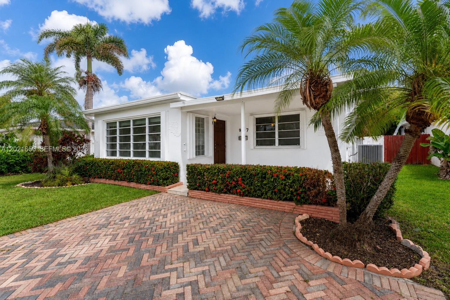 A white single-story house features a brick paver driveway and a landscaped front yard — 947 Lincoln St, Hollywood FL 33019, HOLLYWOOD, FL
