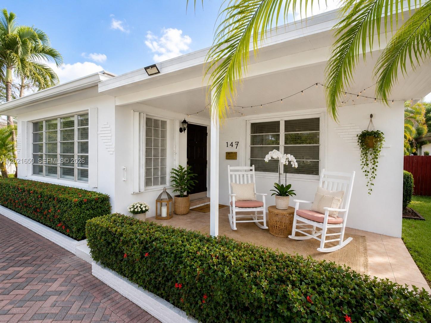 A white house exterior features a covered porch with two rocking chairs and a hedge — 947 Lincoln St, Hollywood FL 33019, HOLLYWOOD, FL